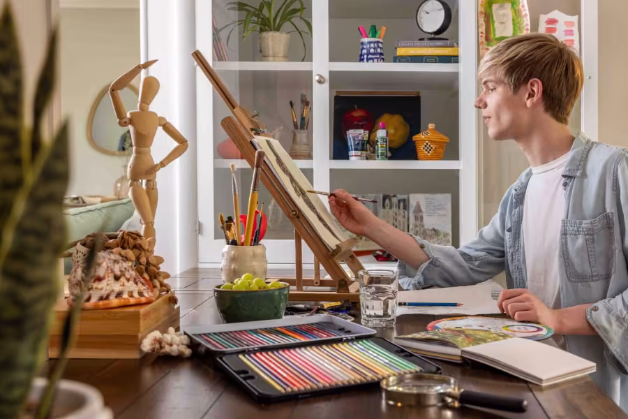 A boy is painting at home with art supplies around him.