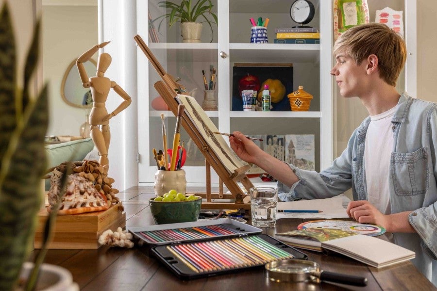A boy is painting at home with art supplies around him.
