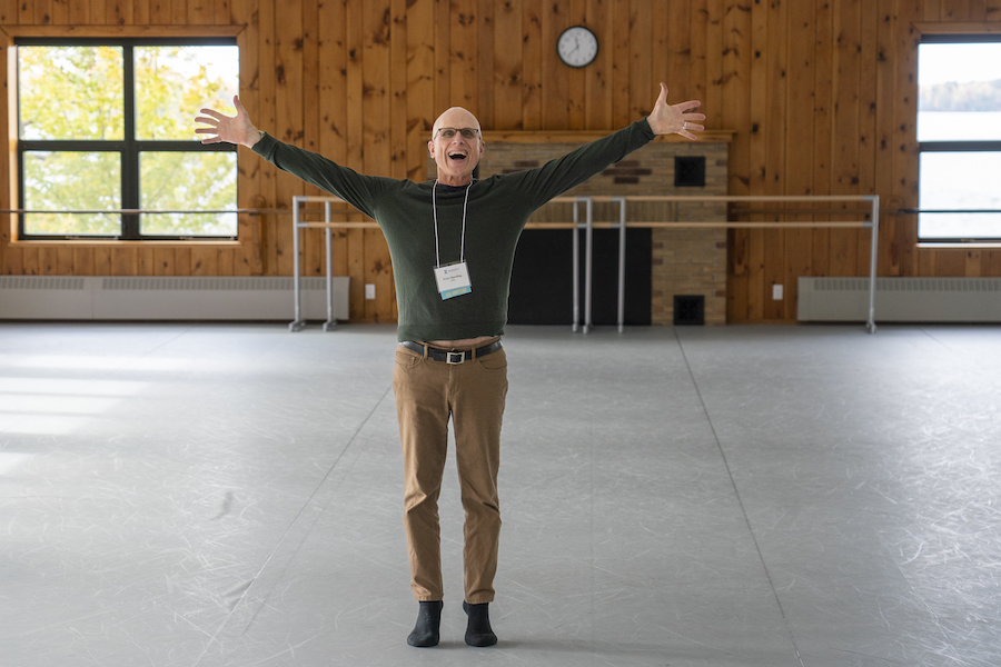 Peter Sparling stands smiling with hands outstretched in the Dance Center. 