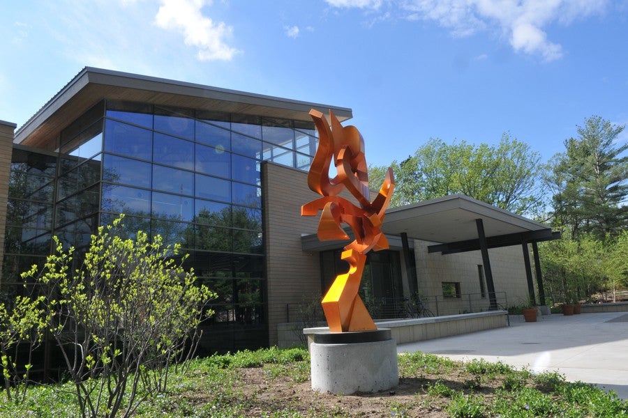 A bright orange metal sculpture stands in front of an impressive arts facility.