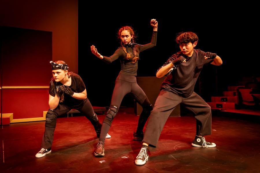Three students dressed in black assume fighting poses.