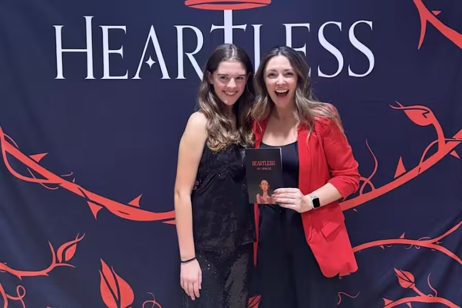 A student and an actress pose in front of a backdrop reading "Heartless."