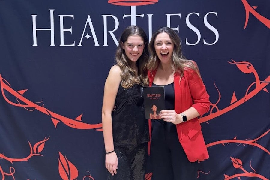 A student and an actress pose in front of a backdrop reading "Heartless."