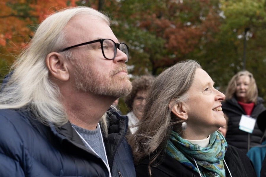 Two people dressed in fall clothing gaze to the side of the camera against a natural backdrop.