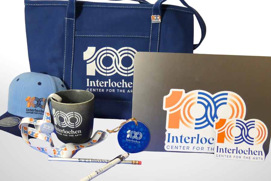Interlochen Center for the Arts 100th anniversary branded merchandise including a tote bag, cap, mug, lanyard, pencils, ornament, and laptop sticker.