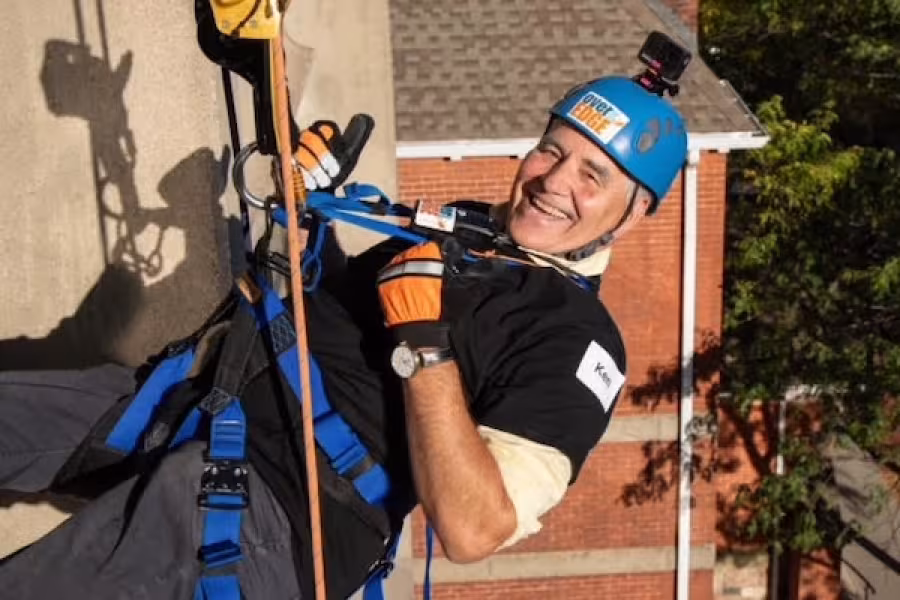 Ken Fischer rappelling down a building, wearing safety gear and a blue helmet.