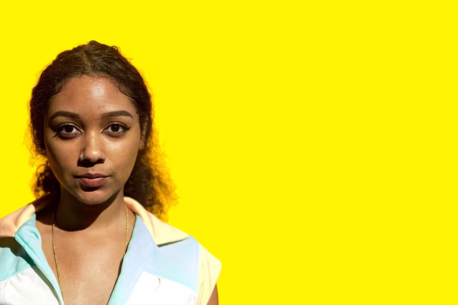Portrait of poet Safia Elhillo against a bright yellow background, facing the camera with soft natural lighting and a calm expression.