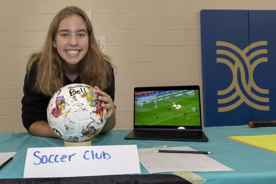 An Interlochen Arts Academy student smiles at the camera and encourages others to sign up for Soccer Club