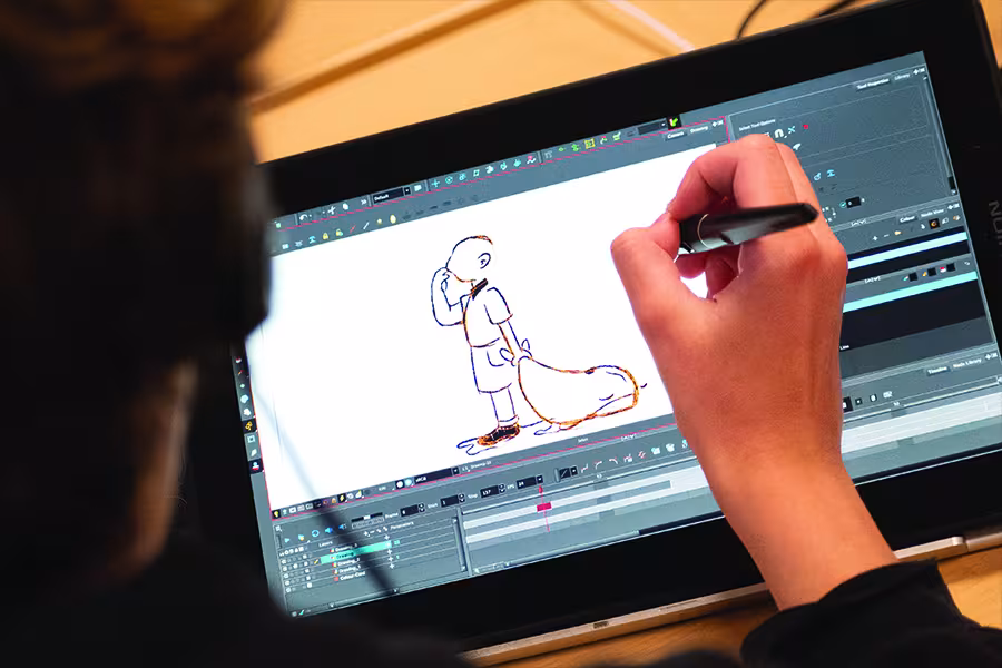 Student uses a stylus to draw a character on a digital animation tablet, creating artwork in animation software displayed on the screen.