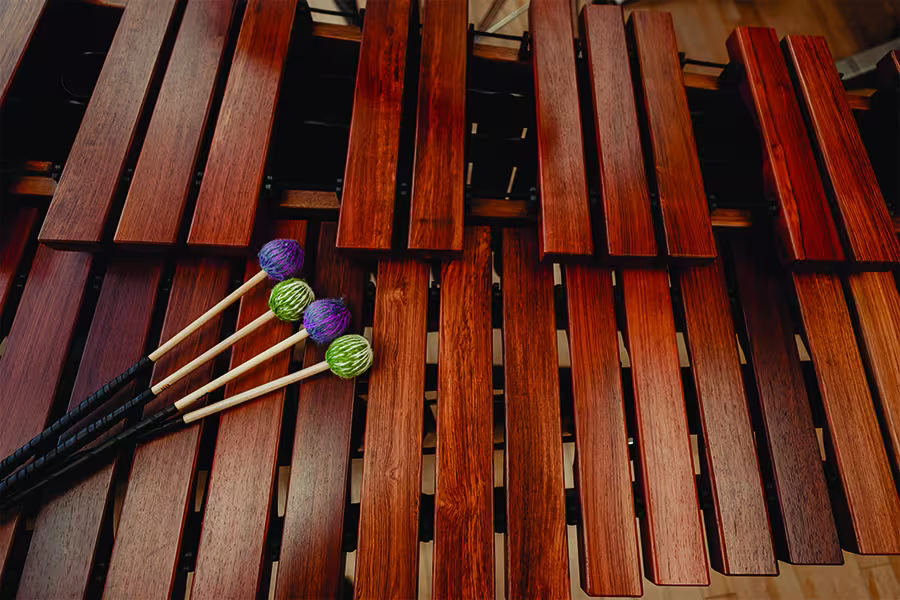 Close-up of the wooden bars of a marimba with four colorful yarn-wrapped mallets resting across the instrument, highlighting the craftsmanship and warm tones of the percussion instrument.