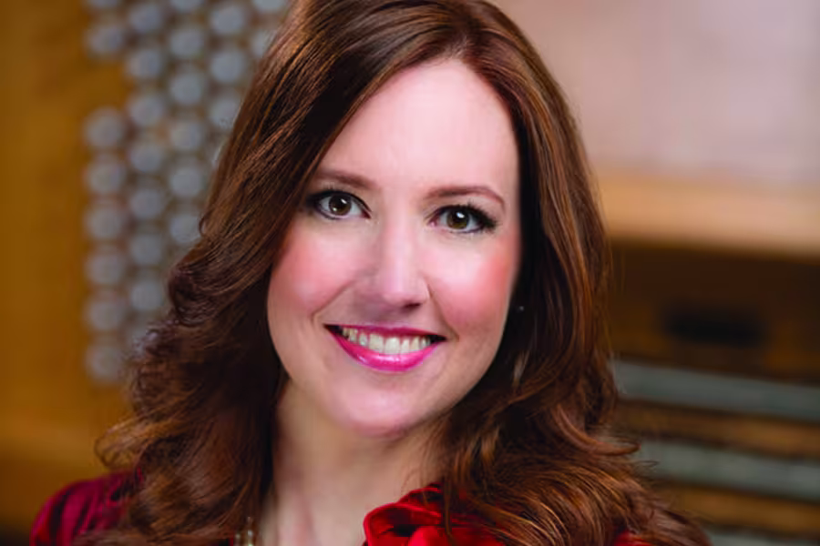 Portrait of organist Christa Miller smiling at the camera, with long brown hair and wearing a red top.