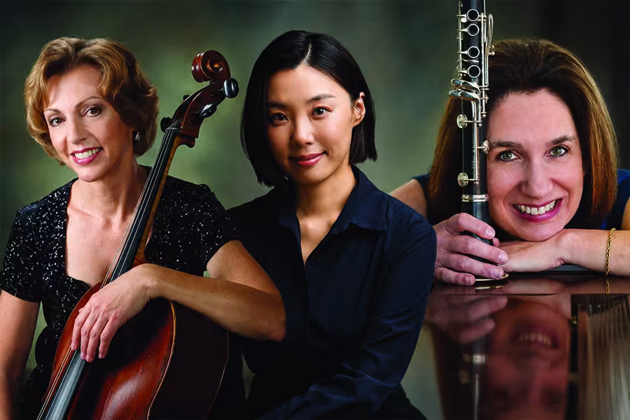 Three female musicians posing with a cello, piano, and clarinet.