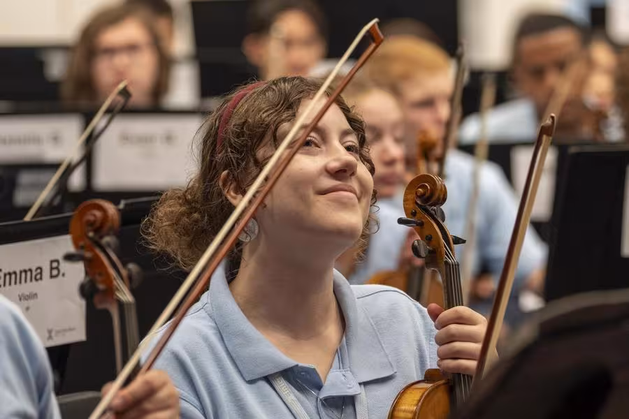 An Interlochen Philharmonic violinist smiles while listening to the conductor. 