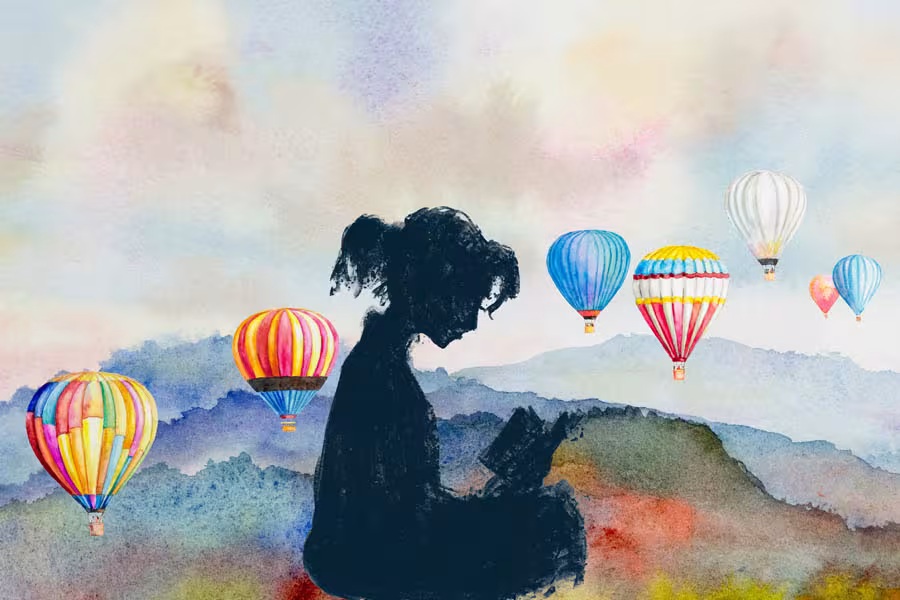 A watercolor-style illustration shows the silhouette of a child sitting and reading a book against a soft landscape of rolling hills. Brightly colored hot air balloons float across the sky, creating a whimsical and imaginative scene that evokes wonder, storytelling, and discovery.