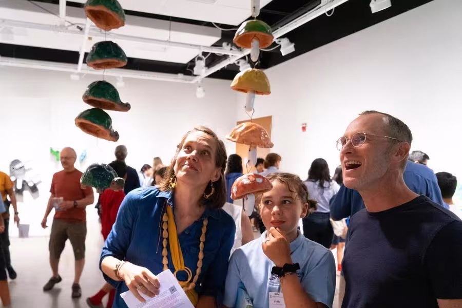 An arts camp student shows their work to their parents