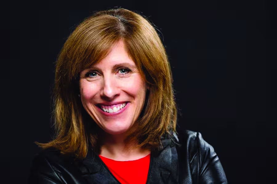 Professional headshot of Lori Sims, a woman with shoulder-length brown hair with bangs, smiling against a dark background while wearing a red shirt under a black jacket.