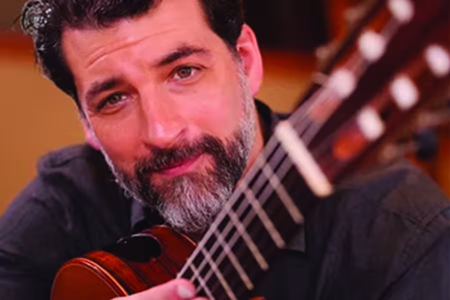 Close-up photo of Matthew Cochran holding a guitar, with the instrument’s neck and strings visible in the foreground.