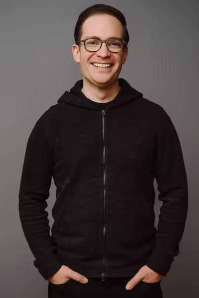 Alumnus Jonathan Slawson wearing a zip up sweatshirt and smiling with his hands in his pockets