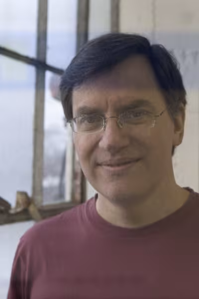Close-up portrait of a Andy Monzina with dark hair and thin-framed glasses, smiling slightly while wearing a maroon crew-neck t-shirt.