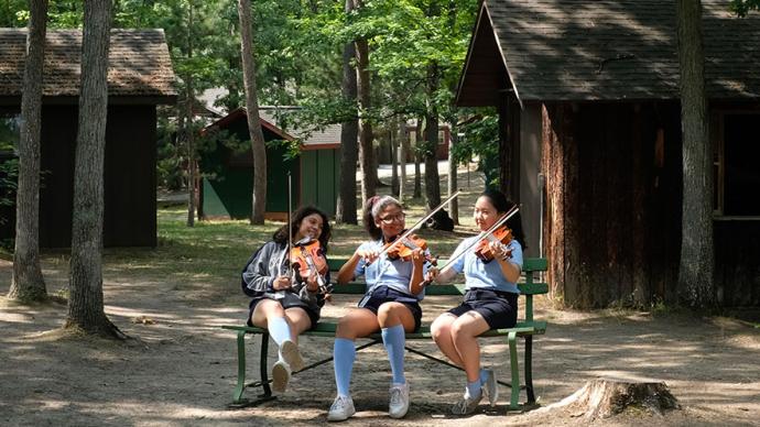 Three violinists rehearse on a bench