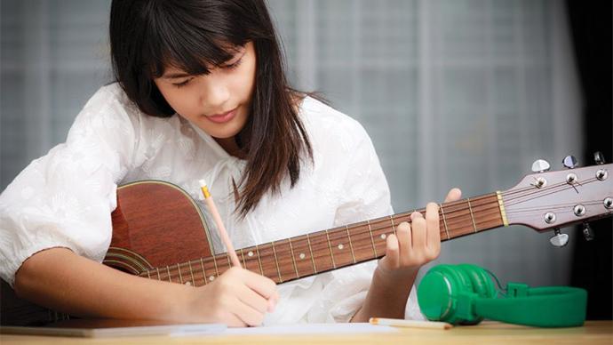 A girl jots down notes while playing guitar