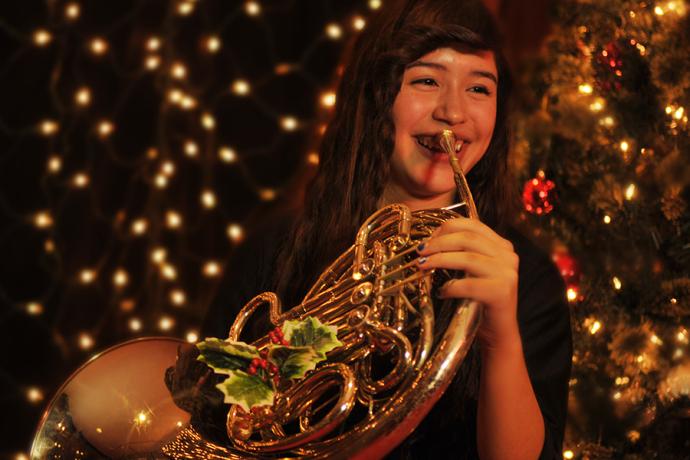 A hornist poses in front of a Christmas tree