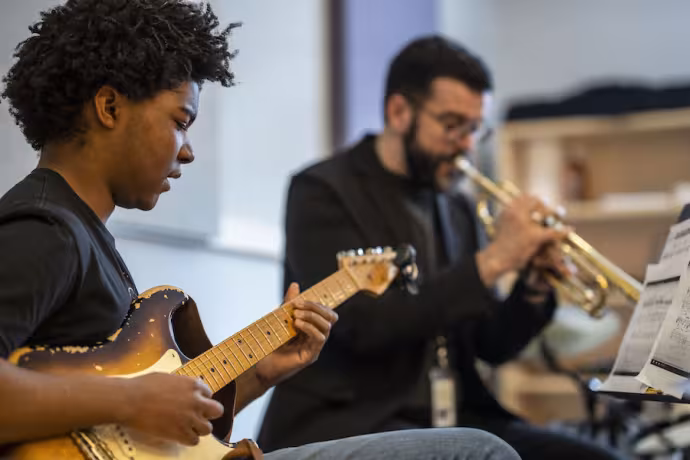 Two students playing music together. One is playing guitar, the other is playing trumpet. 
