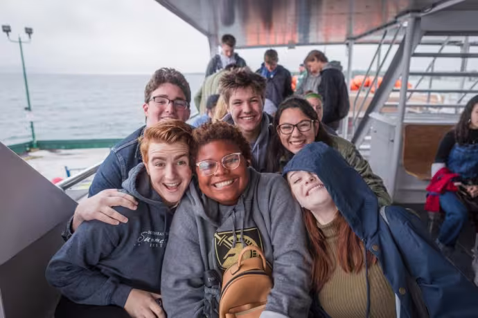 A group of six students smile at the camera from the deck of a ferry.