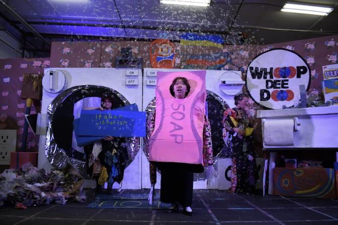 A student dressed as a bar of soap stands in front of a pretend washer and dryer.