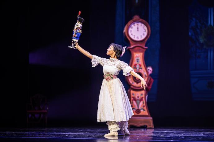 A young girl dressed in white holds up a nutcracker.