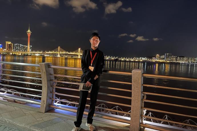 A student dressed in black leans against a bridge overlooking a cityscape at night.
