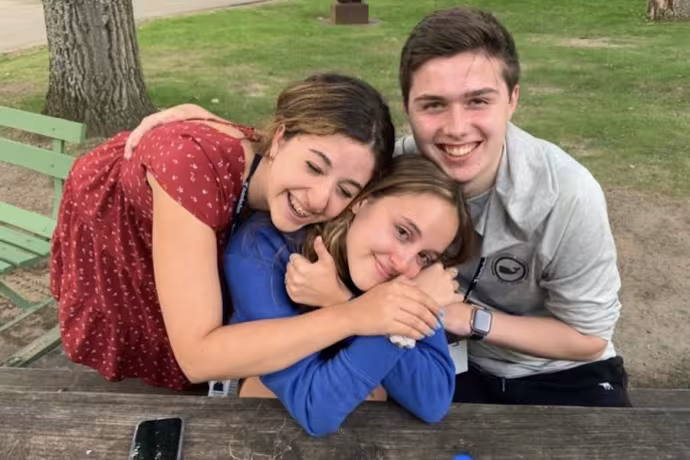 Three students put their arms around each other and smile at the camera.