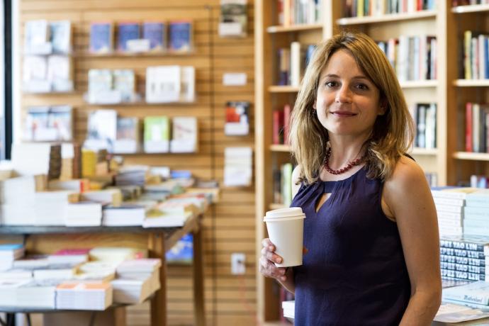 Author Karen Russell poses with a coffee in her hand as she stands in a bookstore.