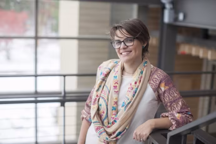 A woman with short brown hair and glasses smiles at the viewer.