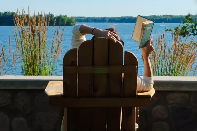 A person reads a book in an Adirondack chair by Green Lake