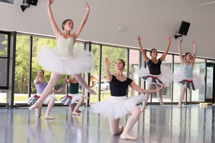 Four young dancers in tutus leap into the air, arms outstretched.
