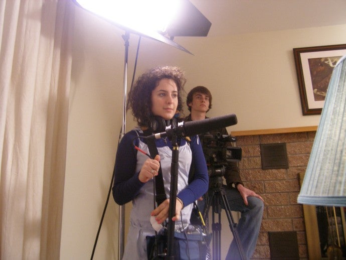 Sarah Nimeh stands behind a microphone on the set of a film. 