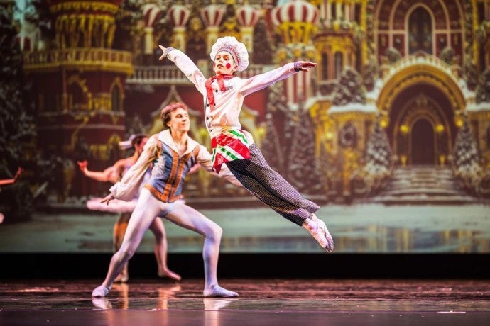 A young dancer dressed as a baker leaps into the air onstage.