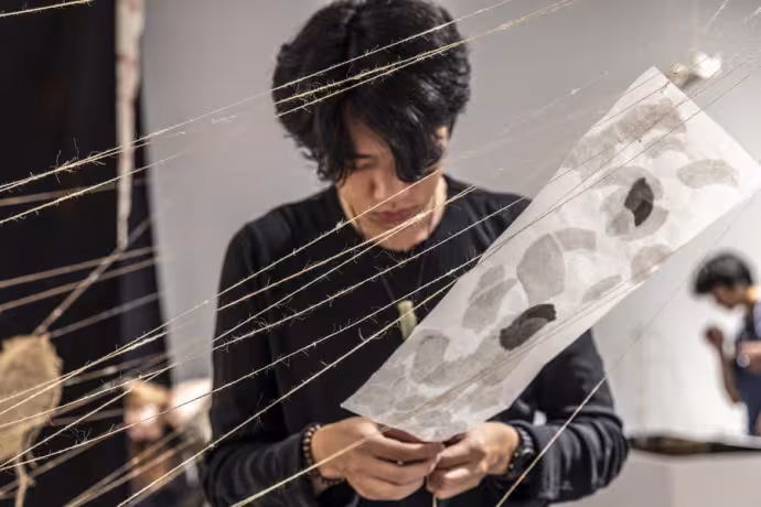 A visual arts student works on an installation with strings and paper.