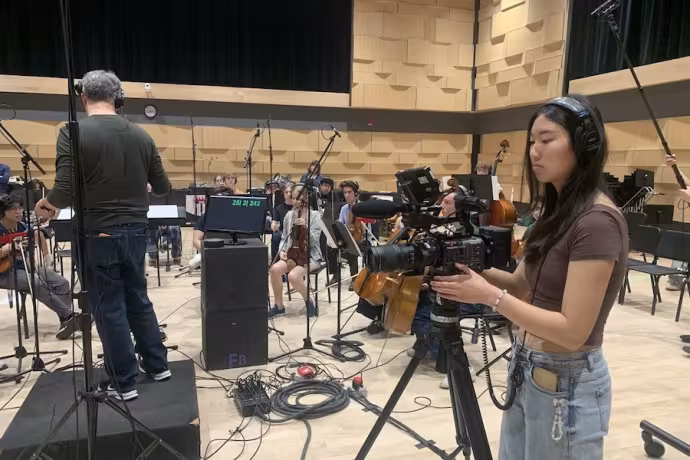 A student with a camera films as an orchestra plays.