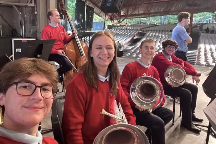 A smiling row of students with brass instruments.