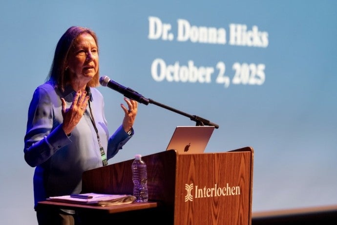 Dr. Donna Hicks, dressed in blue, gestures as she speaks from a podium.