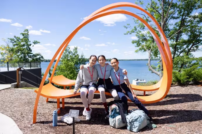 Three students relax on a creatively-designed orange bench