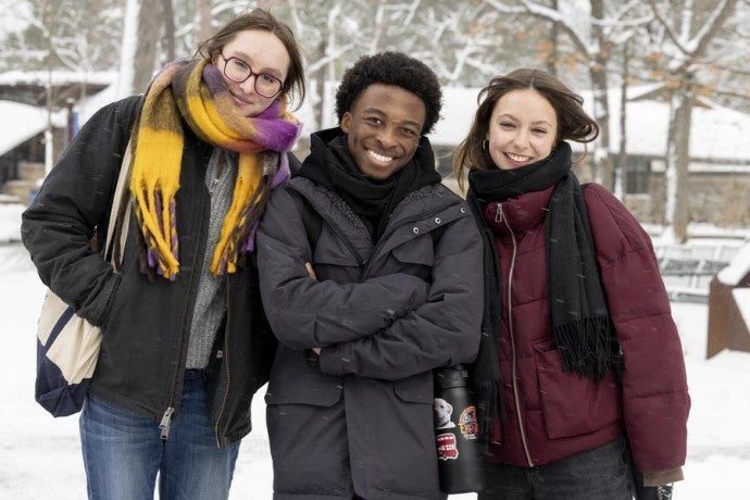 Three warmly-dressed students smile in the snow.