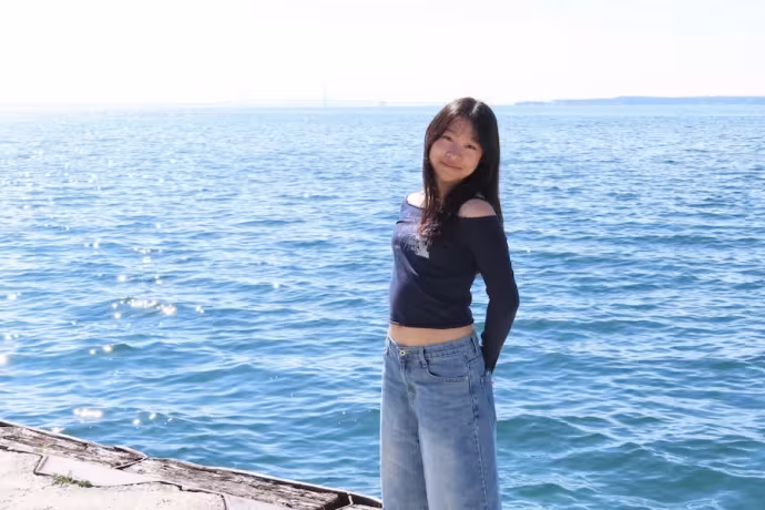 A student poses by the water on a sunny day.