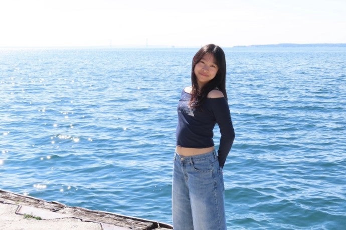 A student poses by the water on a sunny day.