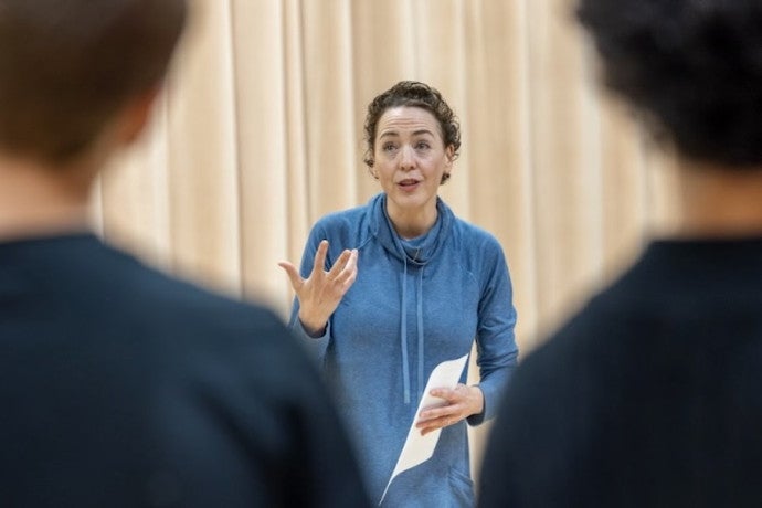 A voice coach gestures excitedly before an audience of students.