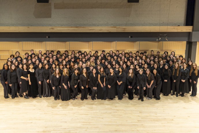 A group of students wearing black pose in a rehearsal room. 