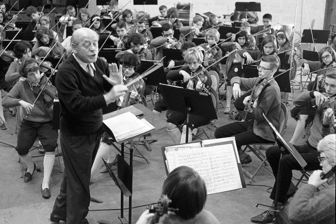 A conductor gestures with his stick to a group of student musicians.