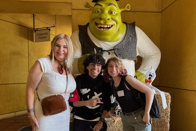 Two students pose witn an instructor in front of a life-size sculpture of Shrek.